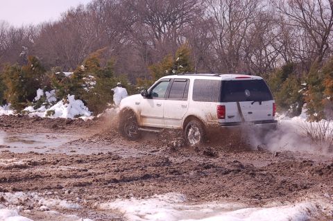 2002 Ford Expedition - A white Ford Expedition navigates a challenging muddy and snowy terrain, kicking up a spray of mud.