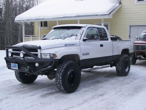 1990 Chevrolet Suburban - A lifted white pickup truck equipped with an aftermarket bumper and off-road tires sits in a snowy driveway next to another vehicle.