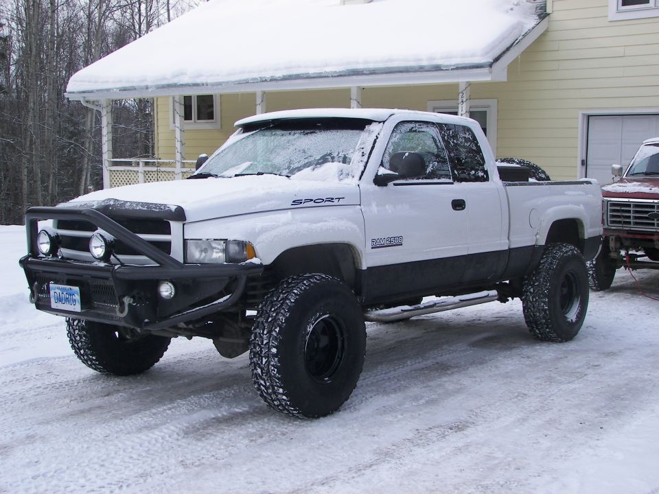 White pickup truck with custom bumper and large tires in snow. 'SPORT' and 'RAM 1500' visible