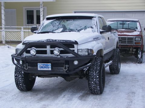 1990 Chevrolet Suburban - A lifted pickup truck with a custom bumper is parked in the snow next to another vehicle.