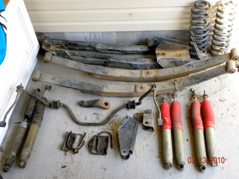 1990 Ford Bronco - A collection of vehicle suspension parts, including leaf springs and shock absorbers, are displayed on a concrete surface.