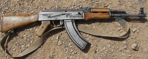 2000 Ford Crown Victoria - AK-47 rifle with wooden furniture and sling is shown on a gravel surface.