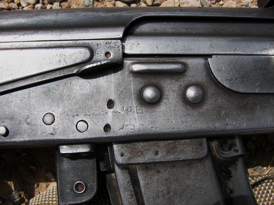 Close-up of a metallic firearm receiver with stamped markings and rivets