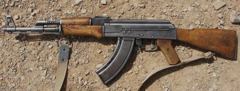 2000 Ford Crown Victoria - AK-47 rifle with wooden furniture and a metal magazine rests on a dirt surface.