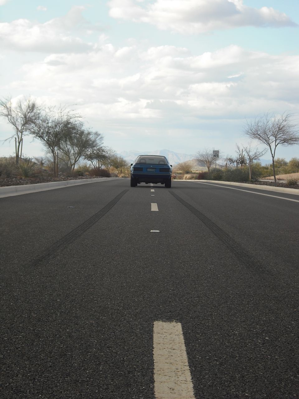 Blue sedan driving away on a two-lane road with tire marks