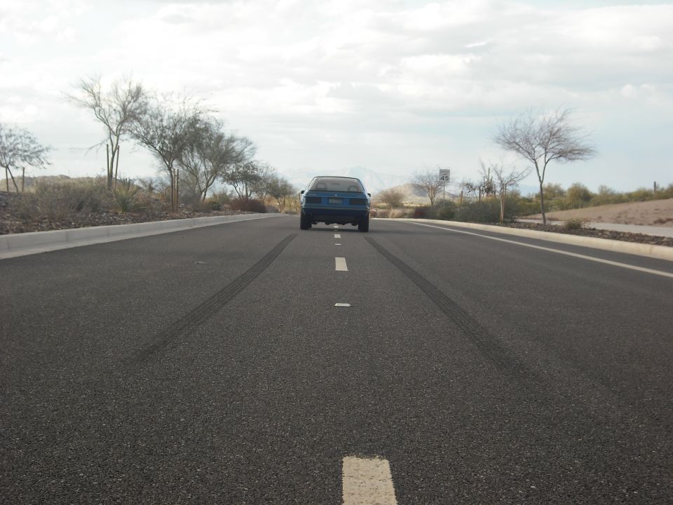 Blue sedan driving away on a road with tire marks behind it
