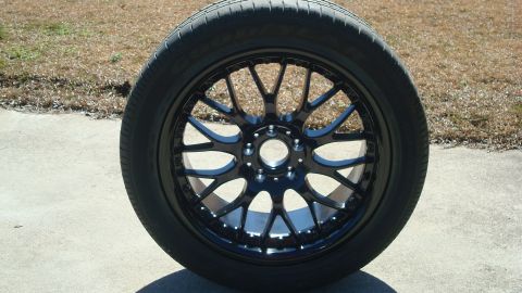 2004 Ford Crown Victoria - A black aftermarket wheel with a tire is displayed outdoors on a concrete surface.