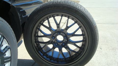 2004 Ford Crown Victoria - Aftermarket wheel and tire assembly shown next to another tire, with a portion of a dark vehicle in the background.