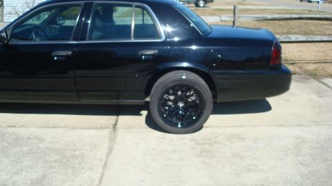 2004 Ford Crown Victoria - This black sedan has custom black rims on the rear wheel and is parked on a concrete surface.