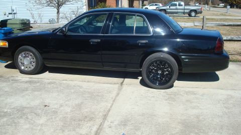 2004 Ford Crown Victoria - A black sedan is parked on a concrete driveway with a house and trees in the background.