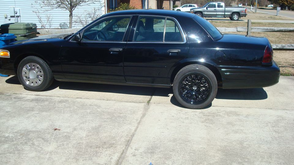 Black sedan parked on concrete driveway, side view. Aftermarket black rims on rear, stock rims on front