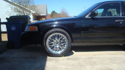 2004 Ford Crown Victoria - Side view of a black 2004 Ford Crown Victoria with custom wheels, parked on a driveway.