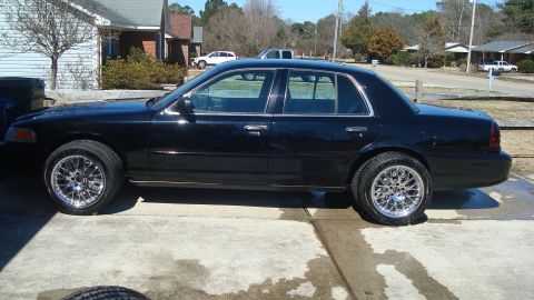 2004 Ford Crown Victoria - A black sedan with chrome rims sits in a concrete driveway in front of a house.