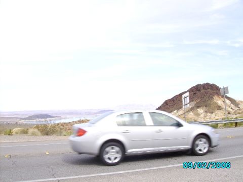 1978 Ford Bronco - Silver sedan driving on a highway with a desert landscape and mountains in the background.