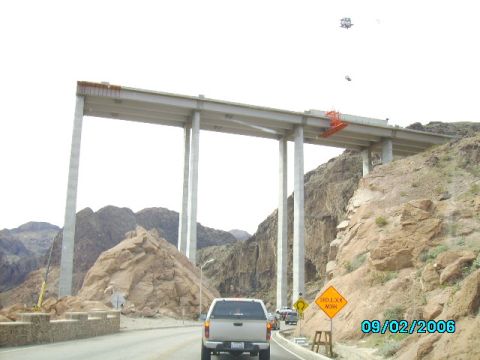 1978 Ford Bronco - A silver pickup truck drives on a road beneath a large bridge under construction, with a "Shoulder Work" sign visible.