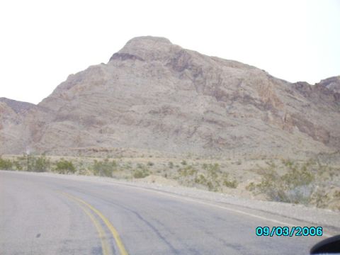 1978 Ford Bronco - A road winds through a dry, arid landscape with large, rocky mountains under a hazy sky.