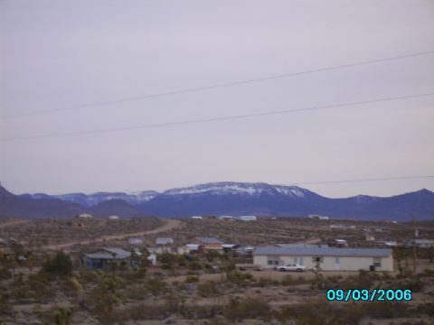 1978 Ford Bronco - A wide shot of a desert landscape with snow-capped mountains in the background and a few buildings and a car in the foreground.