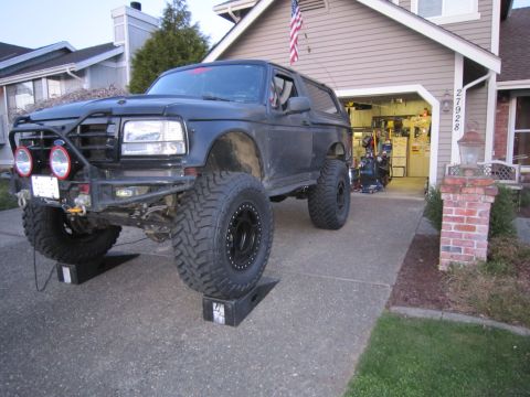 1996 Ford Bronco - This modified Ford Bronco sits on ramps in a driveway, sporting large off-road tires and an aftermarket bumper.