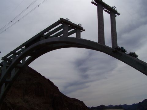 1978 Ford Bronco - A large concrete bridge is under construction, with its arch and towers silhouetted against a cloudy sky.