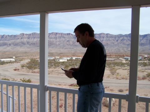 1978 Ford Bronco - A man stands on a porch, looking down at his phone, with a vast desert vista behind him.