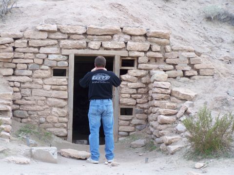 1978 Ford Bronco - A man stands in front of an ancient stone structure, possibly a dwelling or ruin, in a desert landscape.