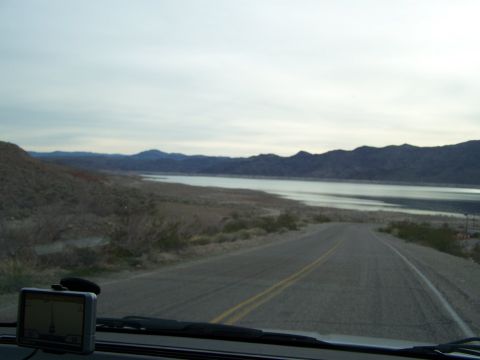1978 Ford Bronco - View from inside a vehicle looking out at a road, lake, and distant mountains under a cloudy sky.