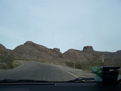 1978 Ford Bronco - A winding road leads through a desolate desert landscape with distinctive rock formations under a hazy sky.