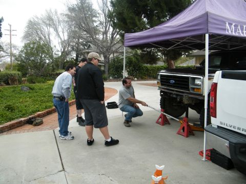 1982 Ford Bronco - Several individuals observe as a lifted truck is supported by jack stands under a canopy.