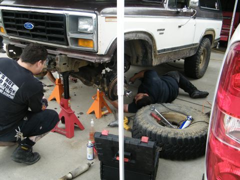 1982 Ford Bronco - Mechanics are working on the front suspension of a lifted Ford Bronco, which appears to be from the early 1980s.