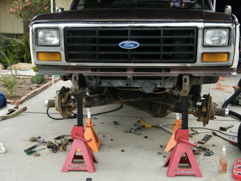 1982 Ford Bronco - Front end of a Ford truck is jacked up for repairs, showing suspension components and tools.