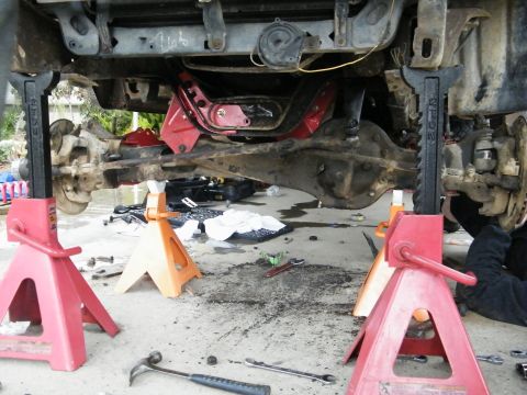 1982 Ford Bronco - Vehicle undercarriage is raised on jack stands for maintenance, revealing suspension and drivetrain parts.