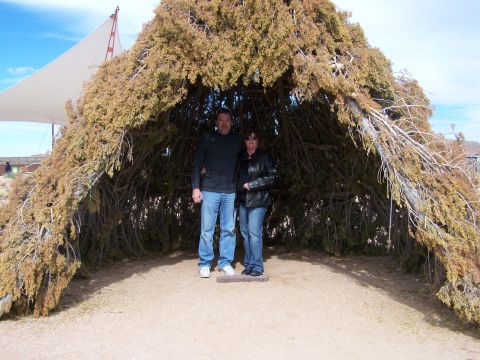 1978 Ford Bronco - A couple poses for a photo inside a rustic, natural shelter constructed from branches and dried vegetation.