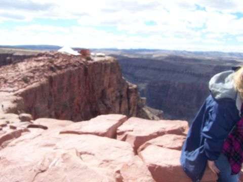 1978 Ford Bronco - A person stands at the edge of a rocky cliff, looking out over a vast canyon under a cloudy sky.