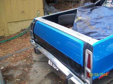 1973 Ford Ranchero - The rear of a Ford Ranchero shows a blue stripe on the black body panel, with a chrome bumper and a spare tire in the bed.