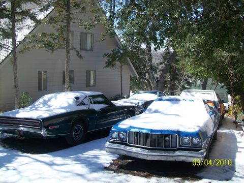 1973 Ford Ranchero - Three vehicles, including a blue 1974 Ford Ranchero GT, sit covered in snow outside a house.