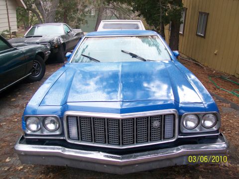 1973 Ford Ranchero - Front view of a blue 1973 Ford Ranchero pickup, showing its distinctive grille and headlights. Another vehicle is visible to the left.