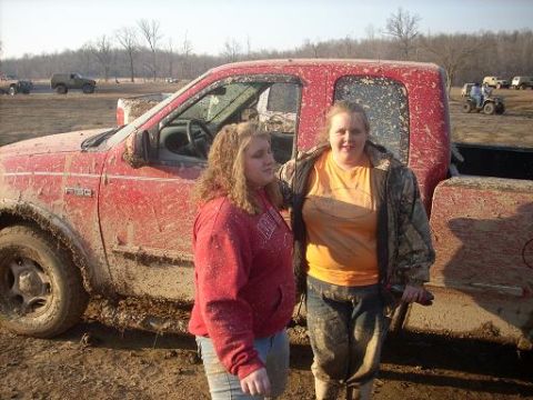1979 Ford Bronco - Two women stand next to a mud-covered red Ford F-150 pickup truck at an outdoor event.