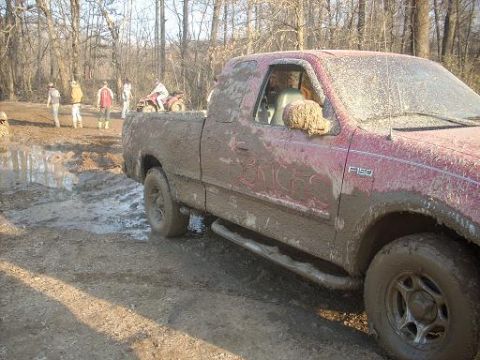 1979 Ford Bronco - A red F-150 pickup truck is caked in mud after driving through a wet, wooded area with several people and an ATV nearby.