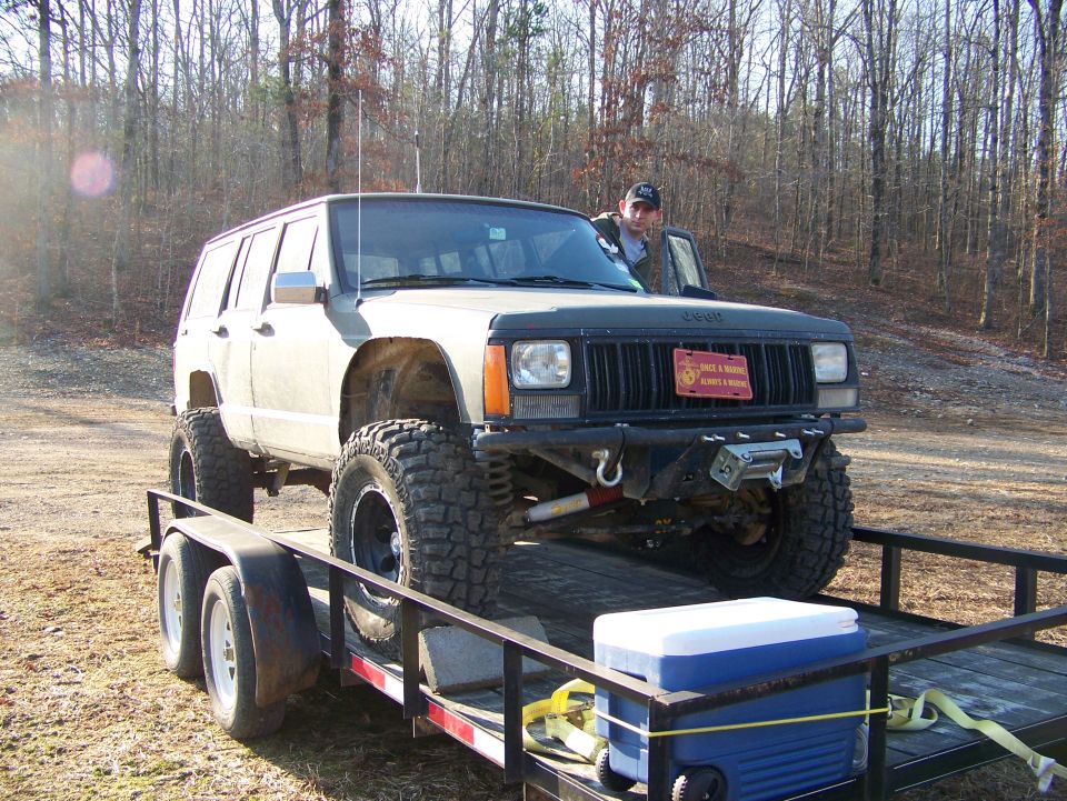 Lifted Jeep Cherokee XJ on a trailer with a man standing in the driver's door