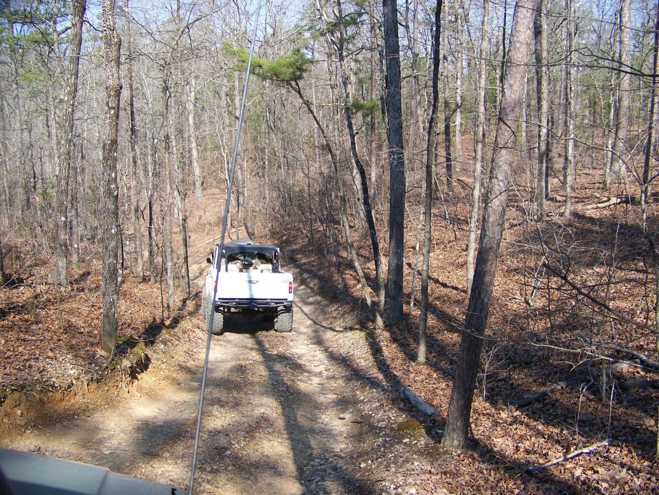 White pickup truck driving on a dirt road through a wooded area
