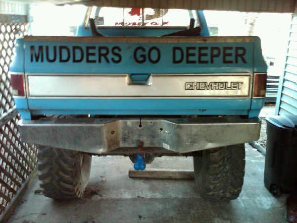 Rear of lifted light blue Chevrolet pickup with 'MUDDERS GO DEEPER' tailgate lettering and big mud tires