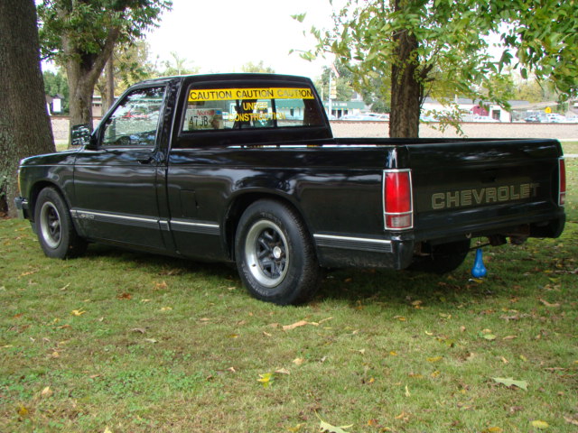 Black lowered Chevy S10 pickup, rear three-quarter view, parked on grass with caution banners in rear window