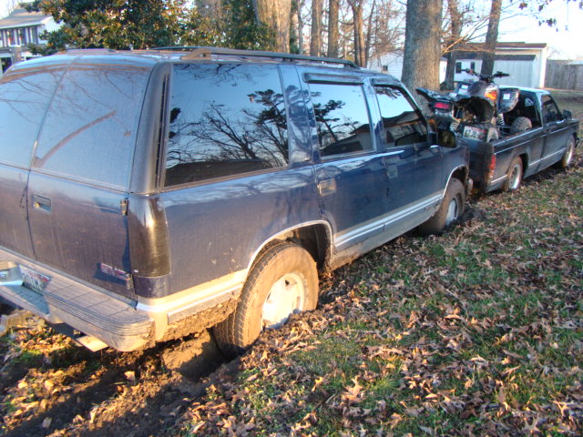 Blue GMC Suburban rear three-quarter parked among trees