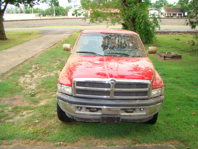 Front view of a red Dodge Ram pickup parked on grass with dirty windshield and chrome grille.