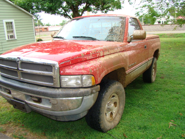 Mud-covered red Dodge Ram regular cab pickup parked on grass, front three-quarter view