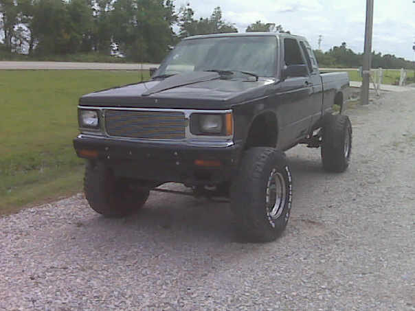 Black lifted GMC extended-cab pickup on gravel with large off-road tires