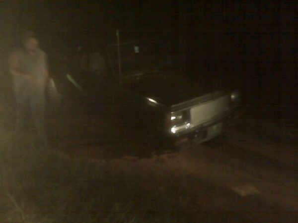Rear view of a dark pickup truck at night on dirt, with a person standing beside it