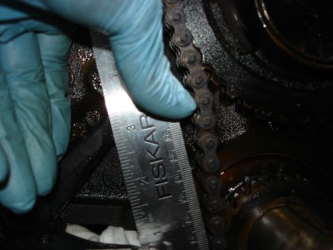 1992 Ford Bronco - A gloved hand uses a ruler to measure an engine timing chain and gears.
