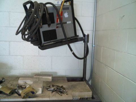 1996 Ford Bronco - A welding machine is mounted on a metal rack against a cinder block wall.