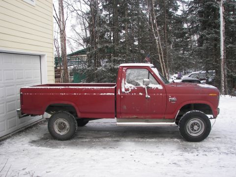1990 Chevrolet Suburban - A red pickup truck sits in the snow, partially obscured by a garage door and trees.